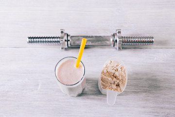 Protein cocktail in a glass, scoop and dumbbell on a white wooden table