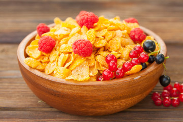 Breakfast of cornflakes with berries in wooden bowl