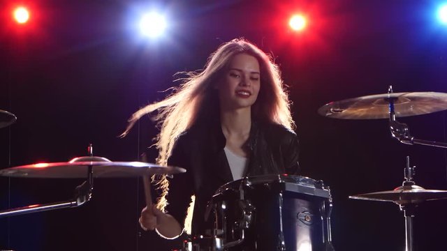 Girl is playing the drums. Black background. Red blue light from behind