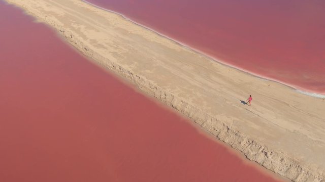 AERIAL: Flying above stunning salt evaporation ponds of Las Coloradas resplendent in gorgeous pink hues in sunny Mexico. Young girl on vacation walking on sandy dunes enjoying view of colorful salinas