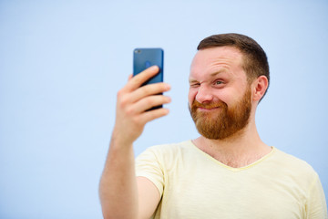 Cheerful bearded Man winks at the phone, suitable for advertising, on a blue background