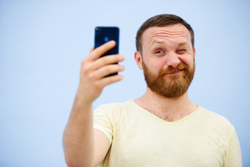 Cheerful bearded Man winks at the phone, suitable for advertising, on a blue background