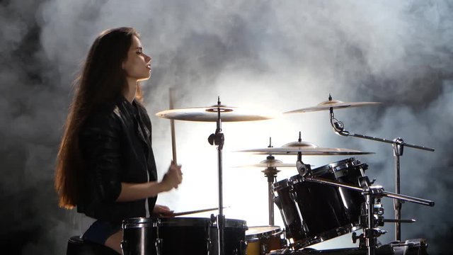 Drummer in a leather jacket plays energetic music. Black smoke background. Side view