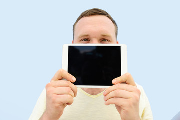 Handsome young man with a beard showing something on the tablet closing the face floor, isolated on a blue background, close-up for your text