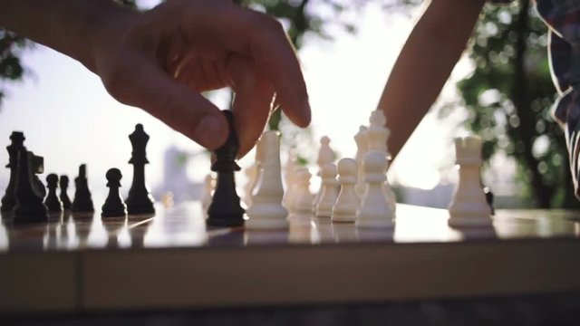 Grandfather and grandson are playing chess in park, slow motion, close up