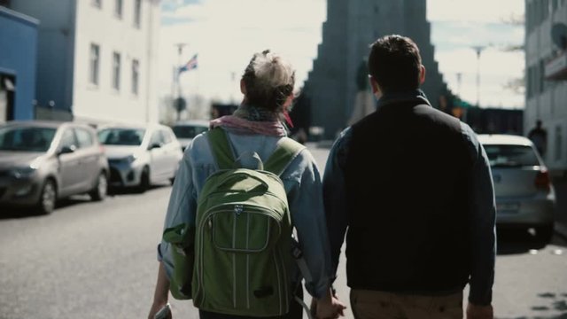 Back view of young stylish couple walking in city centre of Reykjavik, Iceland near the famous Hallgrimskirkja church.