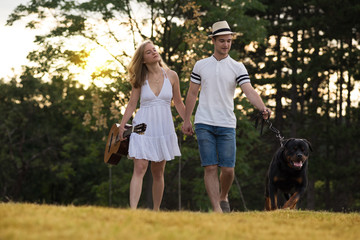 Naklejka na ściany i meble Young couple in love with guitar and dog rottweiler in the nature
