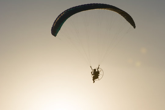 Silhouette of a male paraglider on a paraplan against a background of a sunset in the sky and clouds hovering over the sea. Concept: freedom, loneliness, hobby, sport.