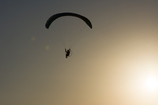 Silhouette of a male paraglider on a paraplan against a background of a sunset in the sky and clouds hovering over the sea. Concept: freedom, loneliness, hobby, sport.