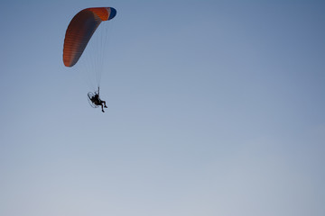 Silhouette of a male paraglider on a paraplan against a background of a sunset in the sky and clouds hovering over the sea. Concept: freedom, loneliness, hobby, sport.