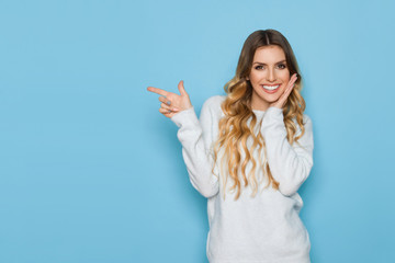 Smiling Young Woman In Pastel Sweater Is Pointing