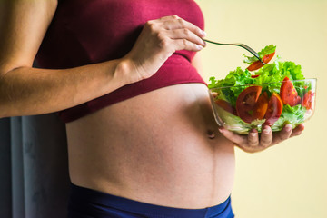 Pregnant woman holding glass bowl with fresh salad