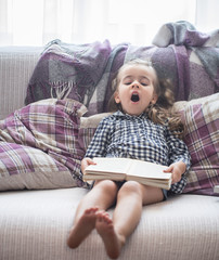 little girl reading book on sofa
