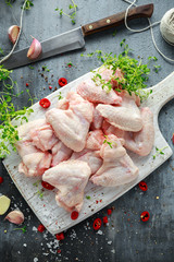 Fresh raw chicken wings on a white cutting board with thyme, chilli, salt, pepper, garlic
