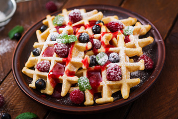 Belgium waffles with raspberries and syrup on a plate.