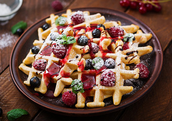 Belgium waffles with raspberries, chocolate and syrup on a plate.