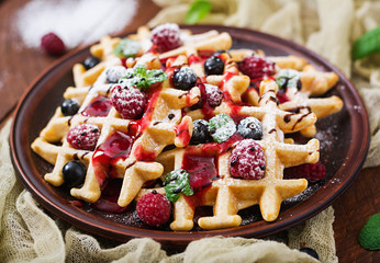 Belgium waffles with raspberries, chocolate and syrup on a plate.