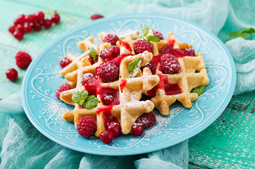 Belgium waffles with raspberries and syrup on a plate.