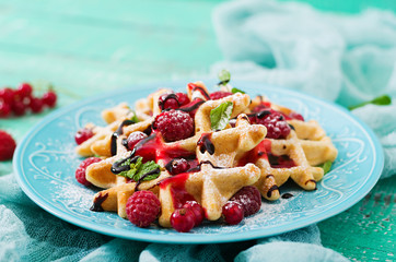 Belgium waffles with raspberries and syrup on a plate.