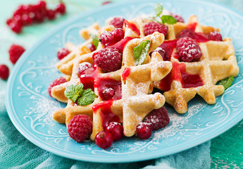 Belgium waffles with raspberries and syrup on a plate.