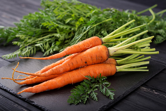 Bunch of fresh carrots with green leaves on  dark  wooden background.