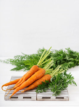 Bunch of fresh carrots with green leaves on  light  wooden background
