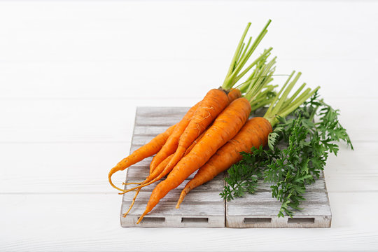 Bunch of fresh carrots with green leaves on  light  wooden background