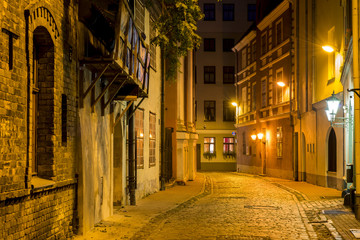 Fototapeta na wymiar Night street in old Riga city, Latvia. Walking through medieval streets of old Riga tourists can feel unforgettable atmosphere of the Middle Ages and unique Gothic architecture