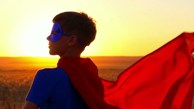 Kid boy dressed in a superman costume staring into the distance at sunset.