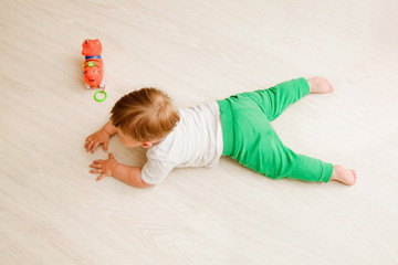 toddler boy white t-shirt and green pants lies on his stomach on the wooden floor. the view from the top