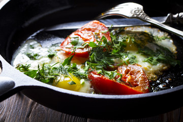 Eggs fried tomatoes in a cast-iron frying pan Wooden vintage background
