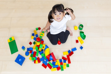 フローリングでブロック遊びをしながら見上げる幼い女の子