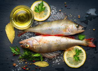 Fresh fish with aromatic herbs, spices, salt. Raw perches on dark slate tray
