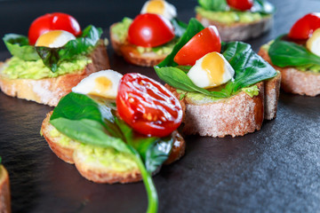 tapas with avocado, boiled quail eggs and Basil with teriyaki sauce on a black granite surface table