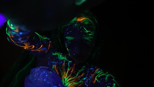 A woman painted with fluorescent paint in the ultraviolet turns the camera