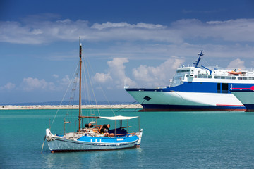 Fototapeta premium A small yacht stands in the port of Zakynthos on the background of a large sailing vessel.