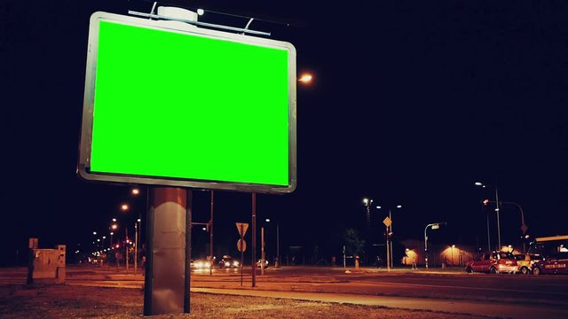 Blank green screen advertising billboard on street at night with traffic time lapse, useful for chroma keying