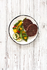 Beefsteaks grilled with vegetables in white plate on a white wood background
