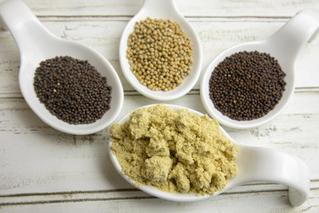 Whole mustard seeds in white china spoons with dry powder