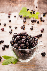 Fresh black currant in the cup and leaves on a wooden table