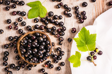 Fresh black currant in the bowl. Many currants and leaves scattered  on the shabby  table. Top view