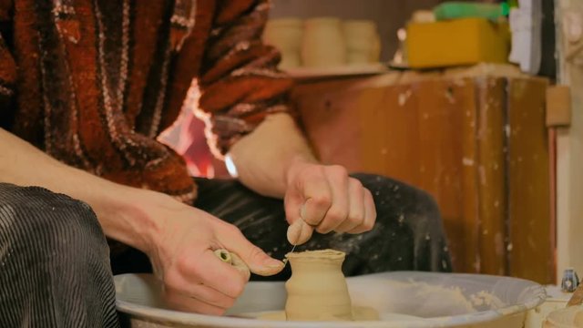 Professional male potter shaping and carving mug with special tool in pottery workshop, studio. Crafting, artwork and handmade concept
