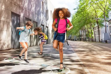 Curly girl with friends jumping hopscotch