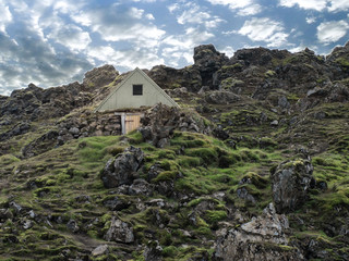 Small traditional rural historical Viking's house in the countryside surrounded with green grass and moss with the blue sky and white clouds above. Iceland, Europe.