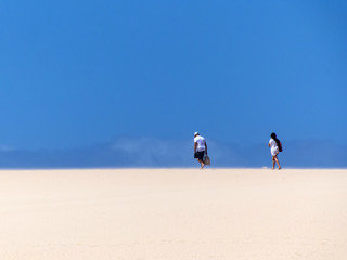 Couple walking over giant sand dunes of Corralejo Fuerteventura in front of a extrem deep blue sky.