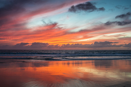 Fototapeta Dramatic red glowing sunset on the beach with water reflections.