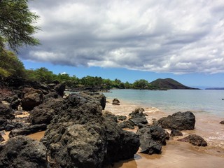 Obraz premium Lava Rock and Coral with Spray of crashing waves in beach tide pools at Maluaka Beach and Kihei Maui with sky and clouds