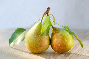 Two pears on one stalk with leaves. With drops of water, lit by the sun on a wooden background. Paired fruit.