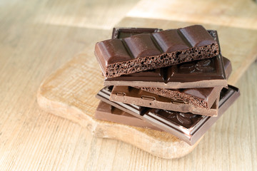 Different broken chocolate bars stacked on a wooden board. Chocolate, lit by the sun. Copy space