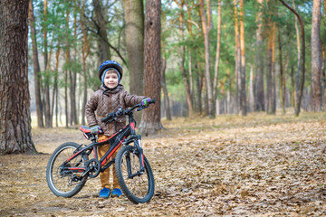 Naklejka premium Happy kid boy of 3 or 5 years having fun in autumn forest with a bicycle on beautiful fall day. Active child wearing bike helmet. Safety, sports, leisure with kids concept.